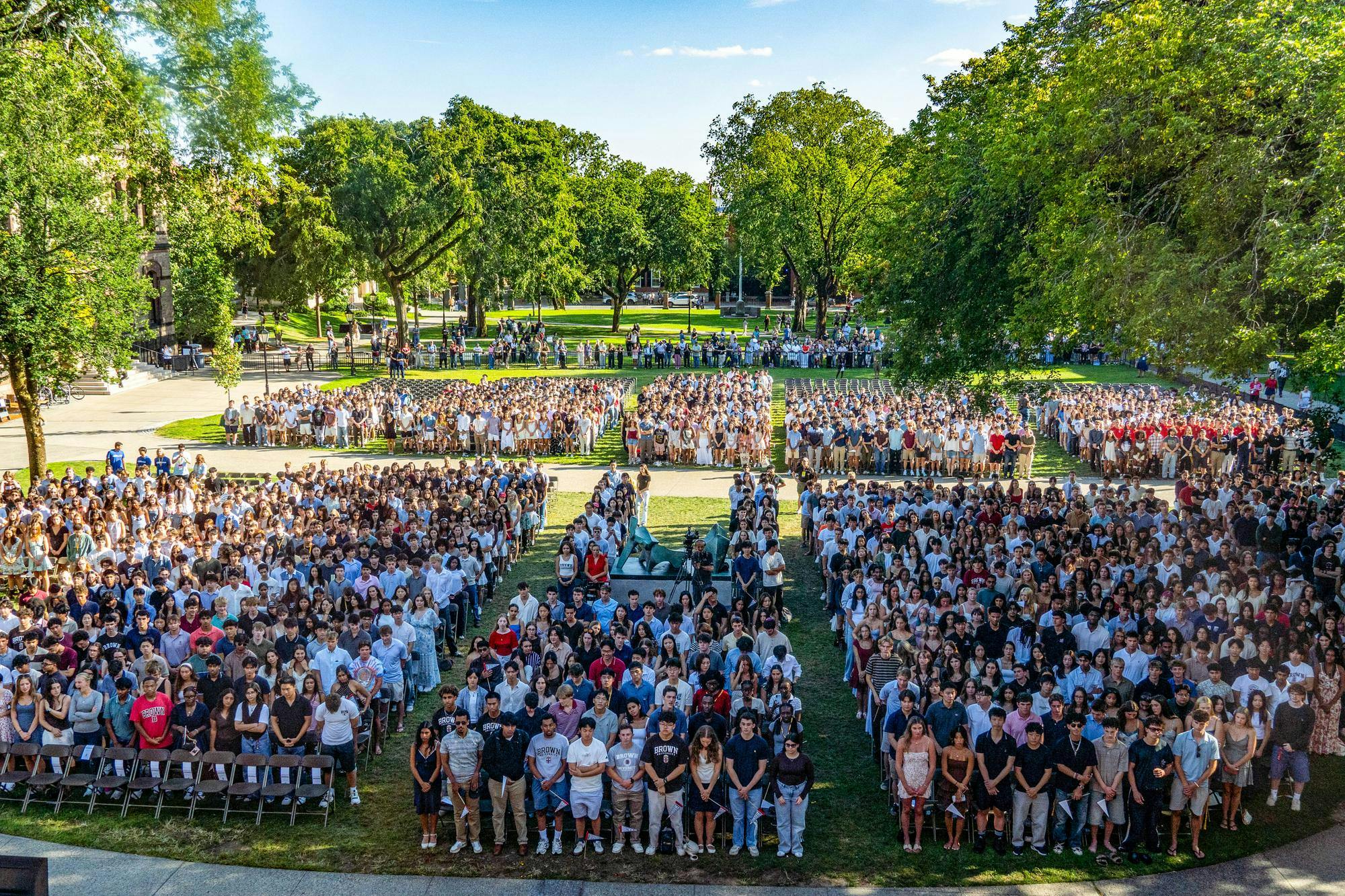 A photo from above depicts the full audience of first-year students standing on the Main Green.
