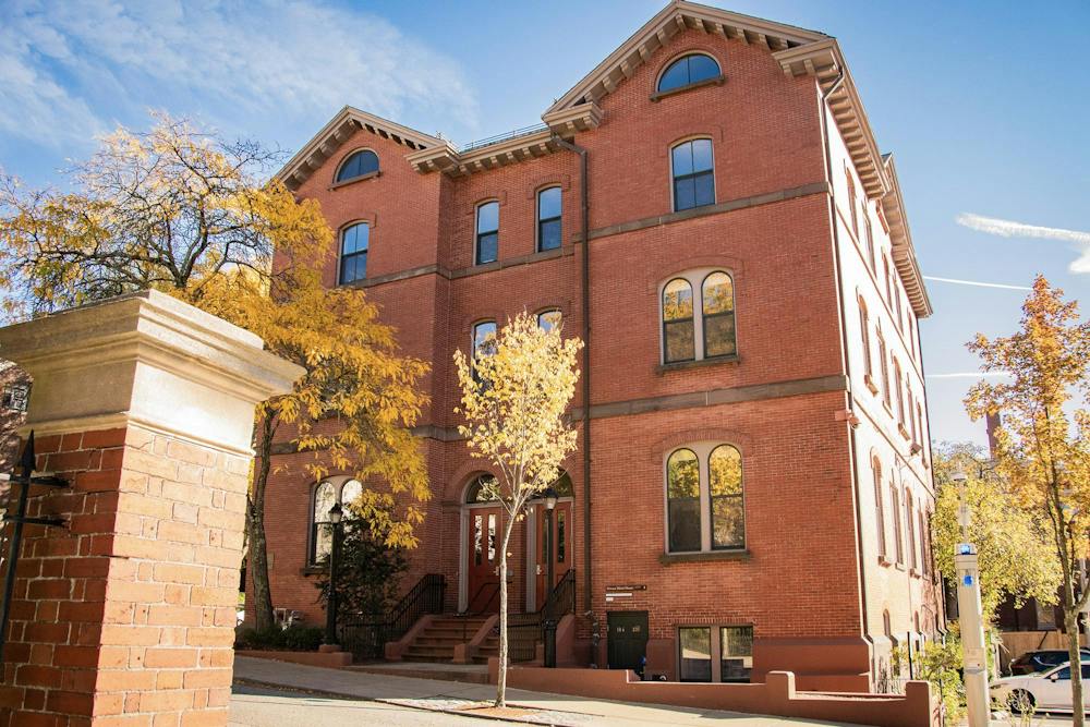 Photo of Huang Horace Mann House: a brick building with two triangle roofs and a staircase from the ground level leading to red doors on a sunny day. 
