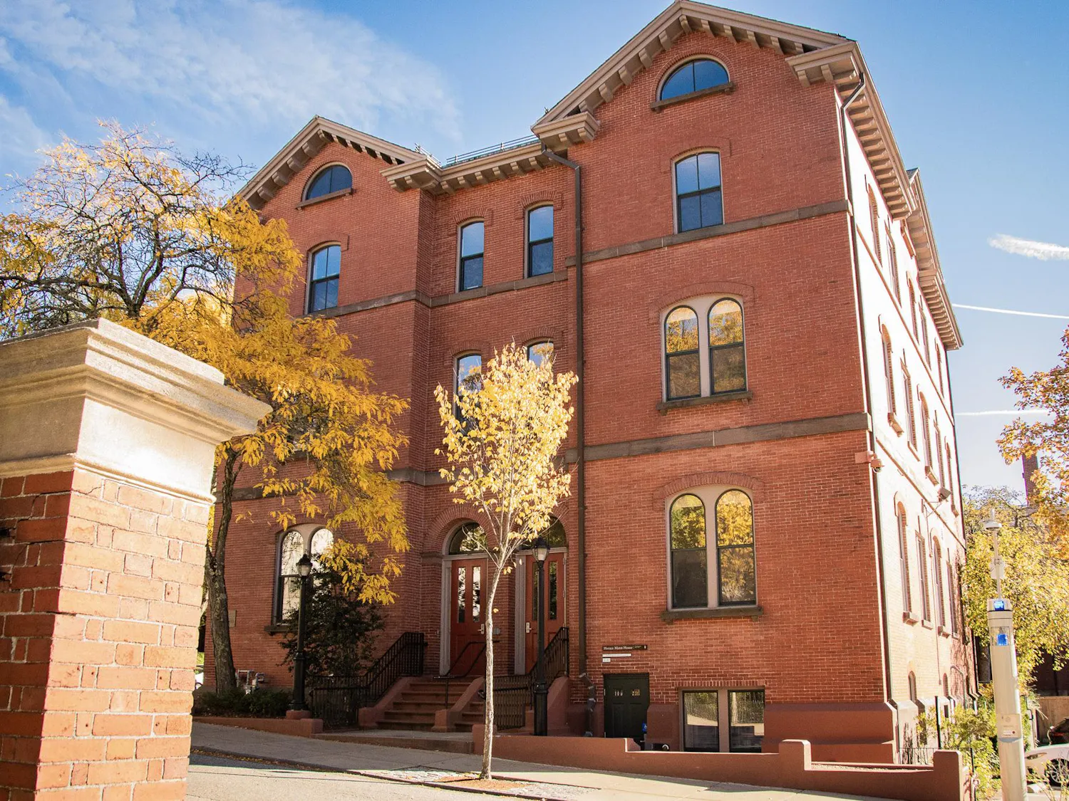 Photo of Huang Horace Mann House: a brick building with two triangle roofs and a staircase from the ground level leading to red doors on a sunny day.