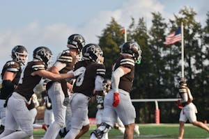 Photo of a group of Brown football players running to the right with the field in the background