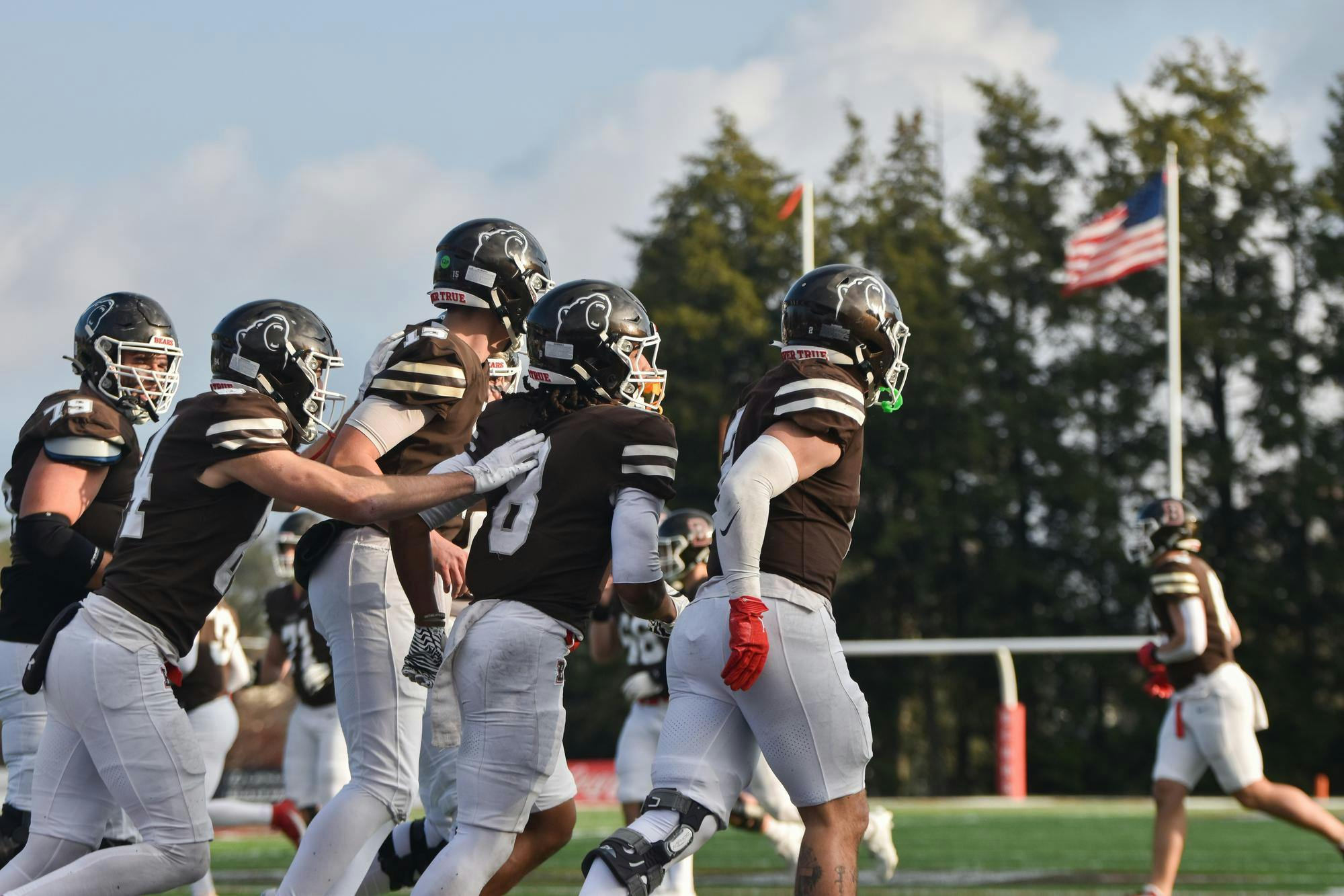 Photo of a group of Brown football players running to the right with the field in the background