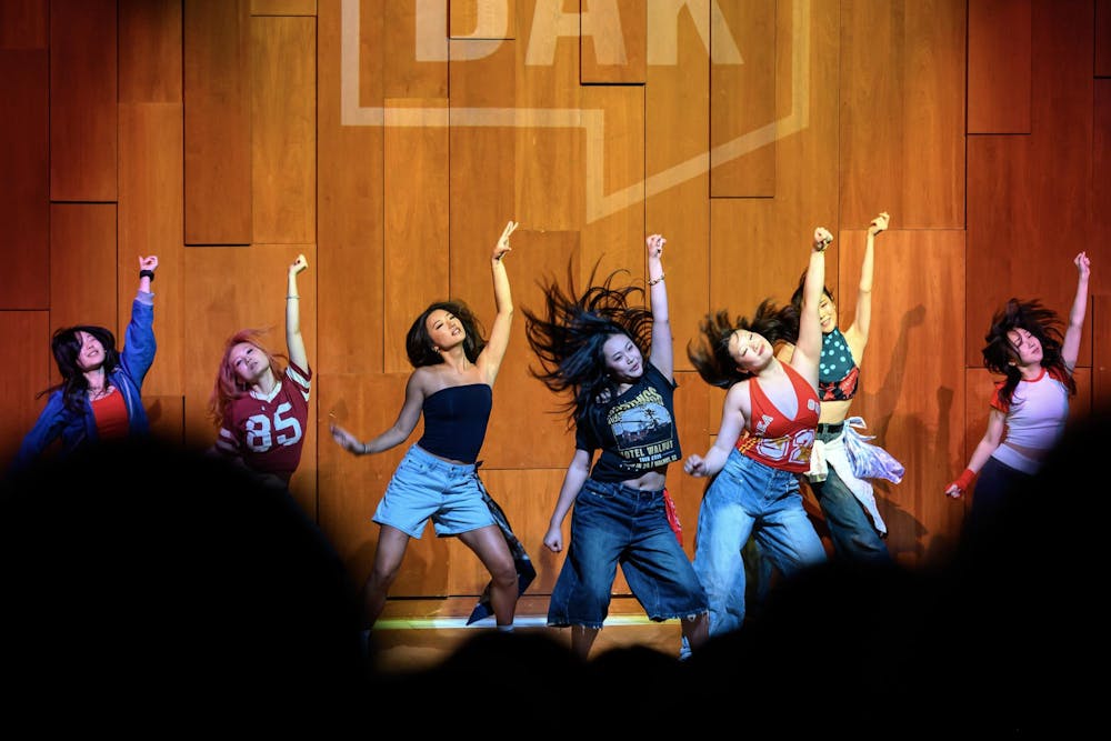 A photo showing girls performing a dance on stage in an auditorium in front of a crowd watching them. 