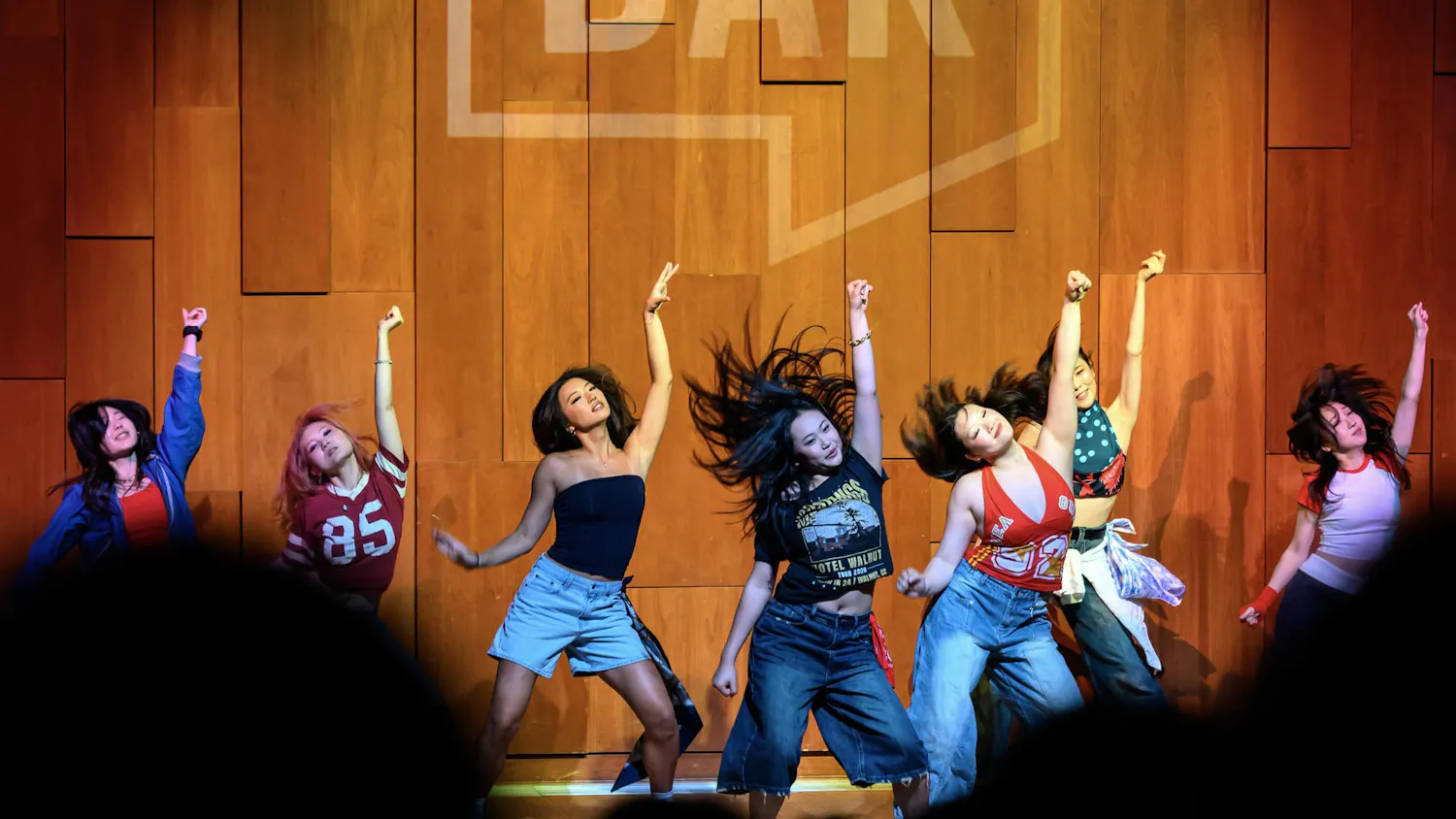 A photo showing girls performing a dance on stage in an auditorium in front of a crowd watching them.