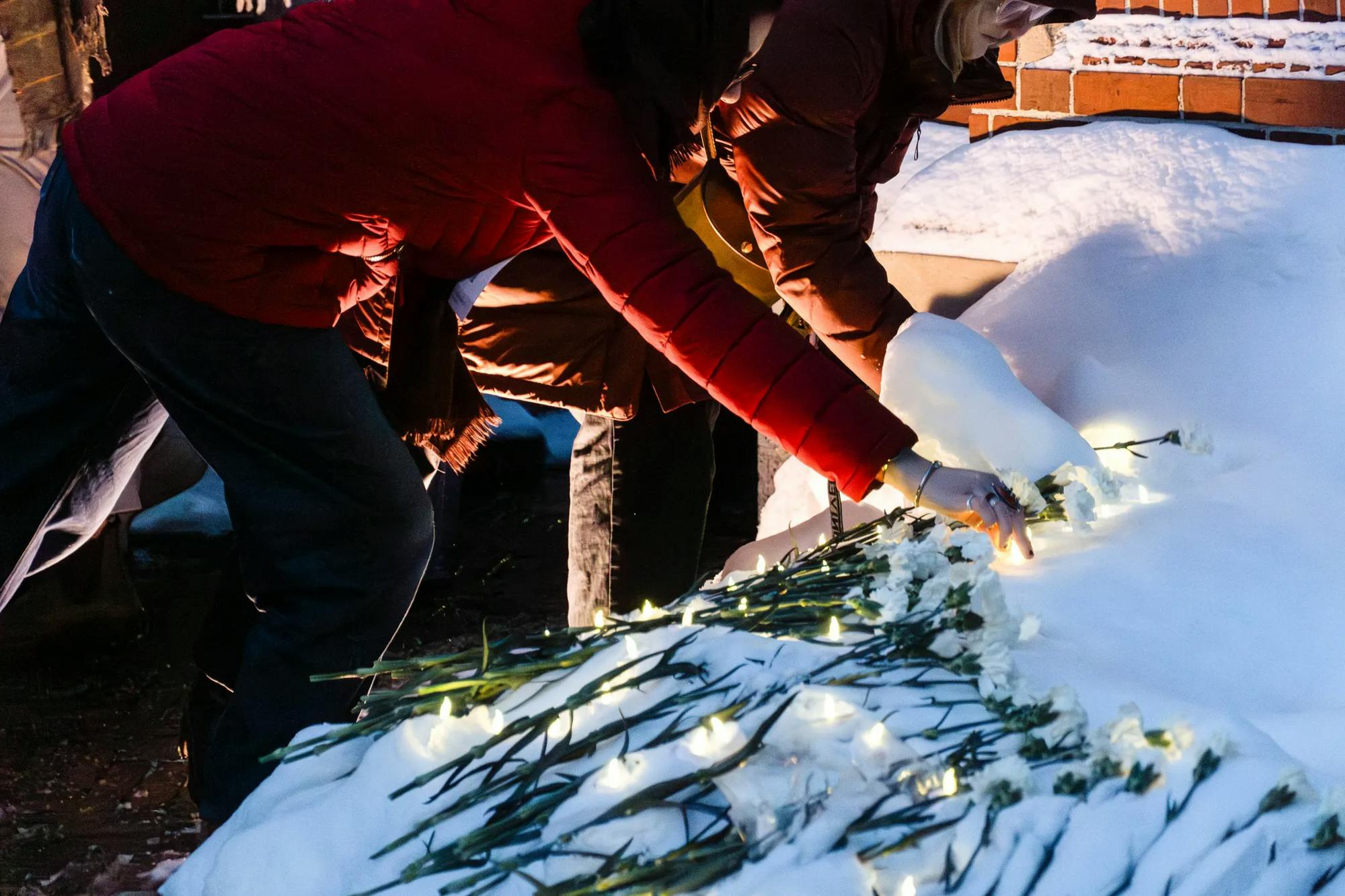 Two individuals in red jackets lay white flowers down at the Van Wickle Gates memorial. 