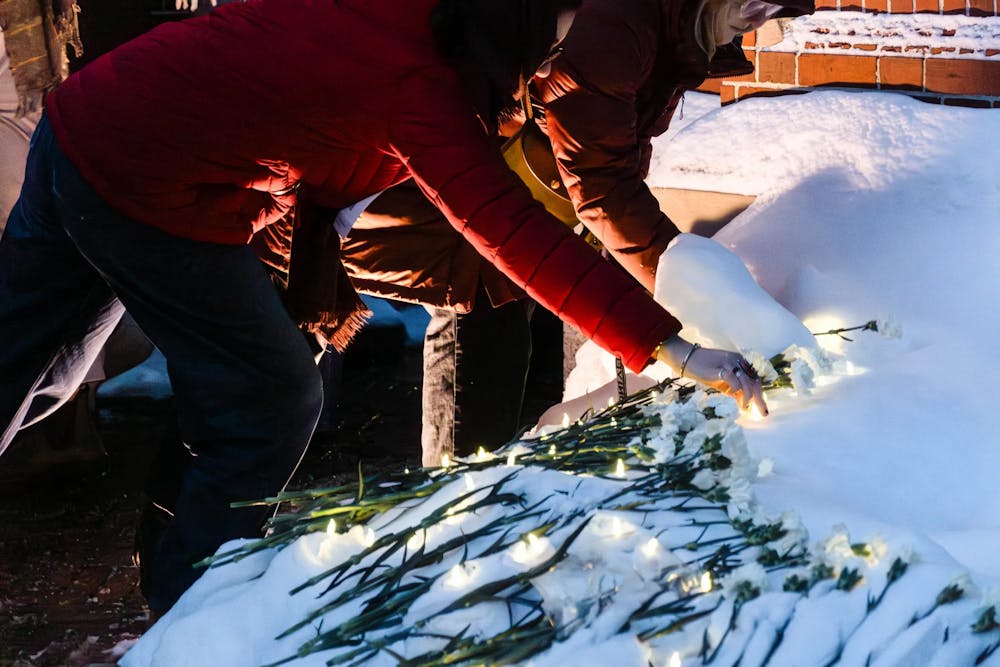 Two individuals in red jackets lay white flowers down at the Van Wickle Gates memorial. 