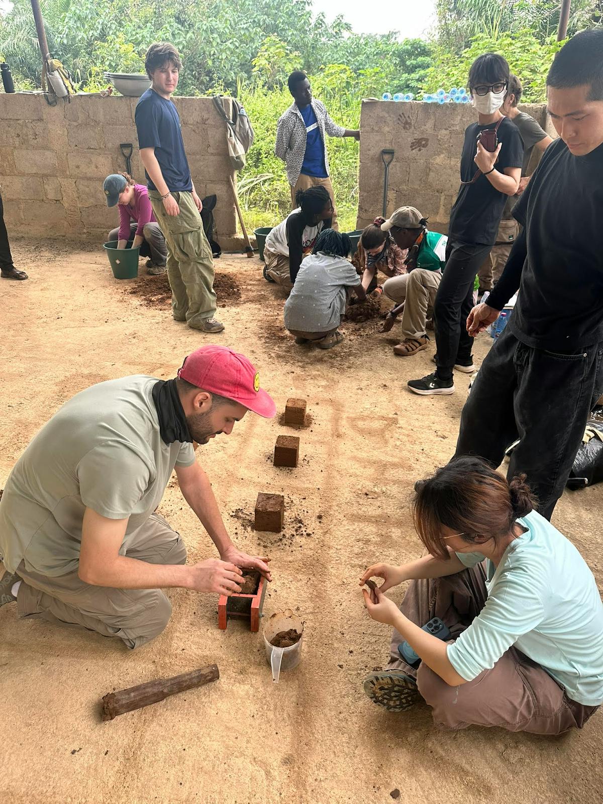 Photo of Brown RISD Dual Degree sitting on the floor making bricks with clay in Ghana.
