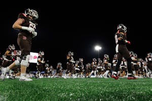 A photo taken from a low angle of many Brown football players walking onto the field. The Jumbotron and a floodlight are visible in the background.  