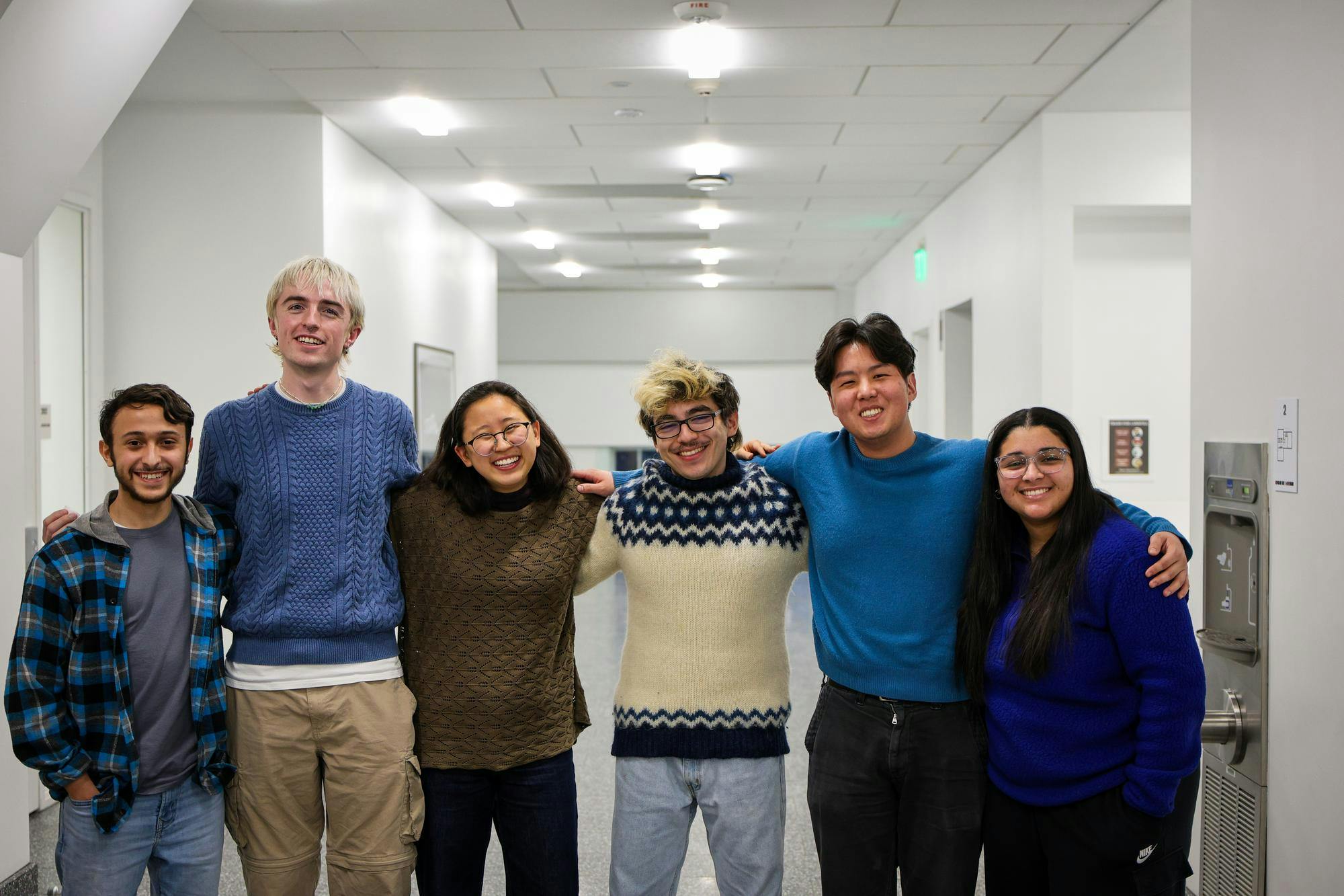 Six individuals stand smiling in a white hallway. 
