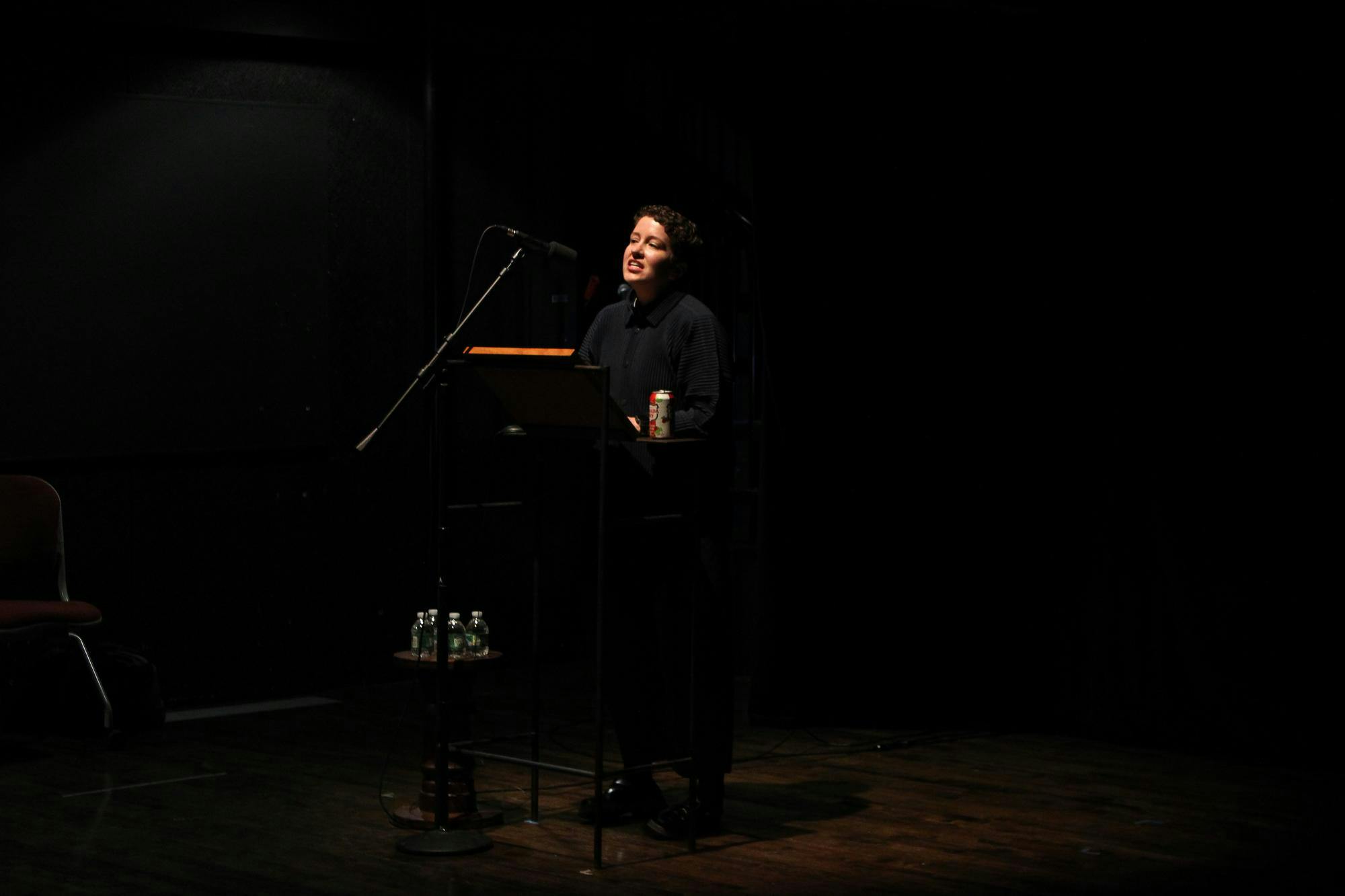 A figure speaking behind a podium in a dimly lit room.