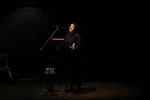 A figure speaking behind a podium in a dimly lit room.