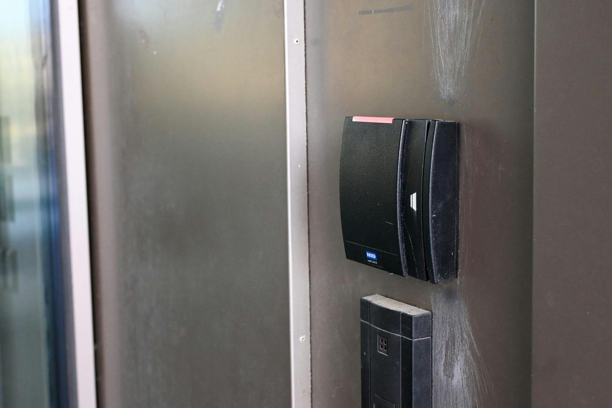 Photo of a black Brown card-swipe reader with a red light against a silver wall background.