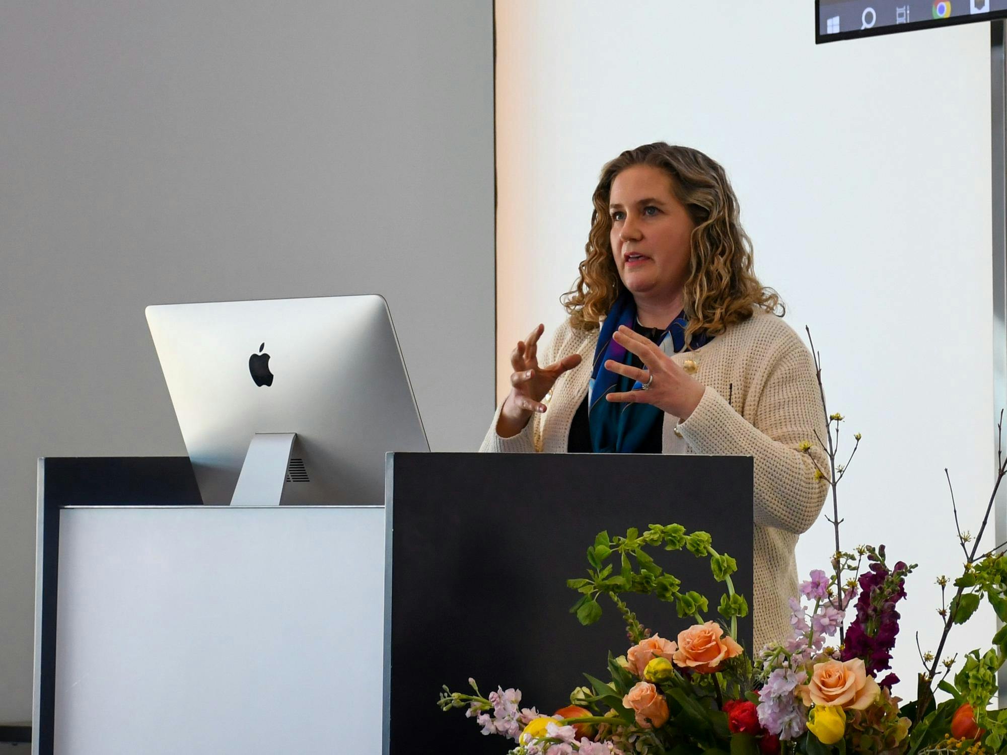 A woman stands in front a computer screen and talks. 