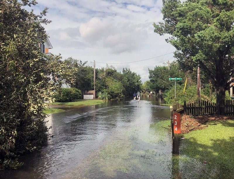 Two islanders ride their bikes through still-wet streets on Friday, Sept. 6, 2019 on Ocracoke Island, N.C., in the aftermath of Hurricane Dorian. (Connie Leinbach/Ocracoke Observer via AP)