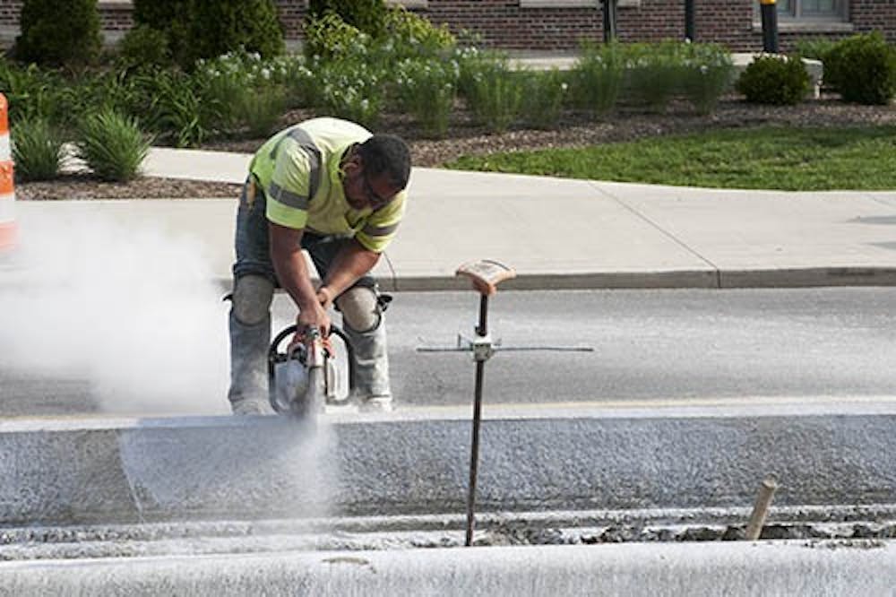 A construction worker uses a saw to create a drainage line in the curb on Riverside Avenue. The construction project’s aim is to expand the median and add more crosswalks and ramps on the section of the street. DN PHOTO JORDAN HUFFER