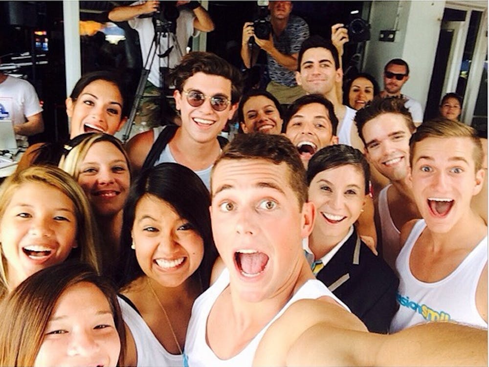 <p>Alumnus Mark E. Miller, center, takes a selfie with #MissionSmile members and Indiana University student Ethan Hethcote. The couple broke the Guinness World Record for selfies taken with strangers in an hour with 355. PHOTO COURTESY OF <a href="http://instagram.com/markemiller7715">MARK E. MILLER'S INSTAGRAM</a></p>