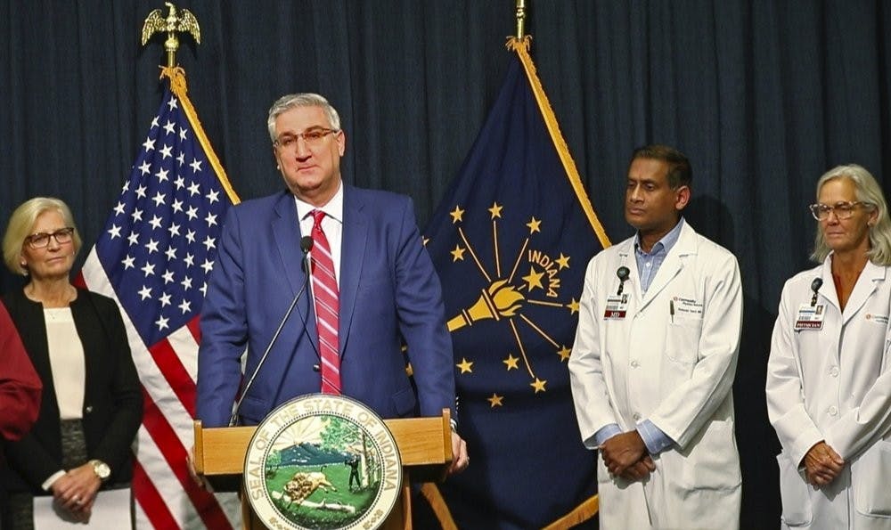 Indiana Gov. Eric Holcomb announces during a press conference at the Indiana Statehouse, Friday, March 6, 2020, in Indianapolis, that the first case of COVID-19 has been diagnosed in the state. Kristina Box, left, Indiana State Health Commissioner, and doctors from Community Health Network stand behind him. (Kelly Wilkinson/The Indianapolis Star via AP)