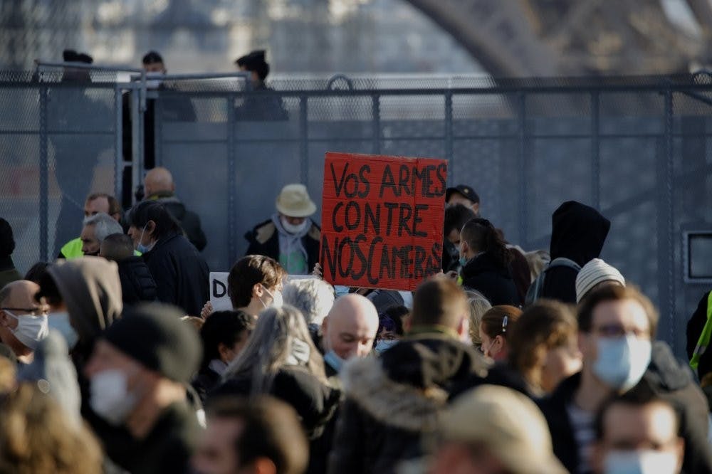 Demonstrators gather during a protest against a bill on police images, in Paris, Saturday, Nov. 21, 2020. Thousands of people took to the streets in Paris and other French cities Saturday to protest a proposed security law they say would impinge on freedom of information and media rights. The board reads: Your guns against our cameras. (AP Photo/Christophe Ena)