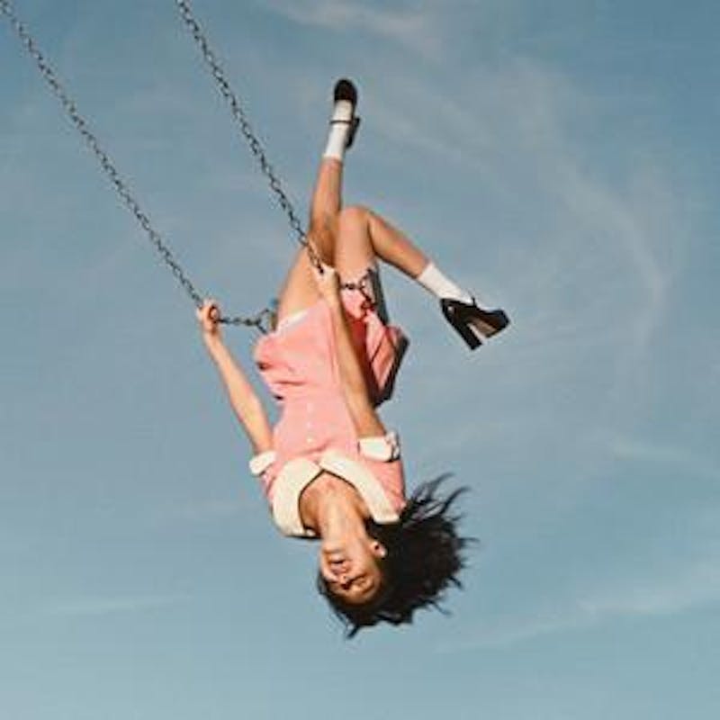 Olivia Rodrigo is wearing a pink dress and sitting on a swing.