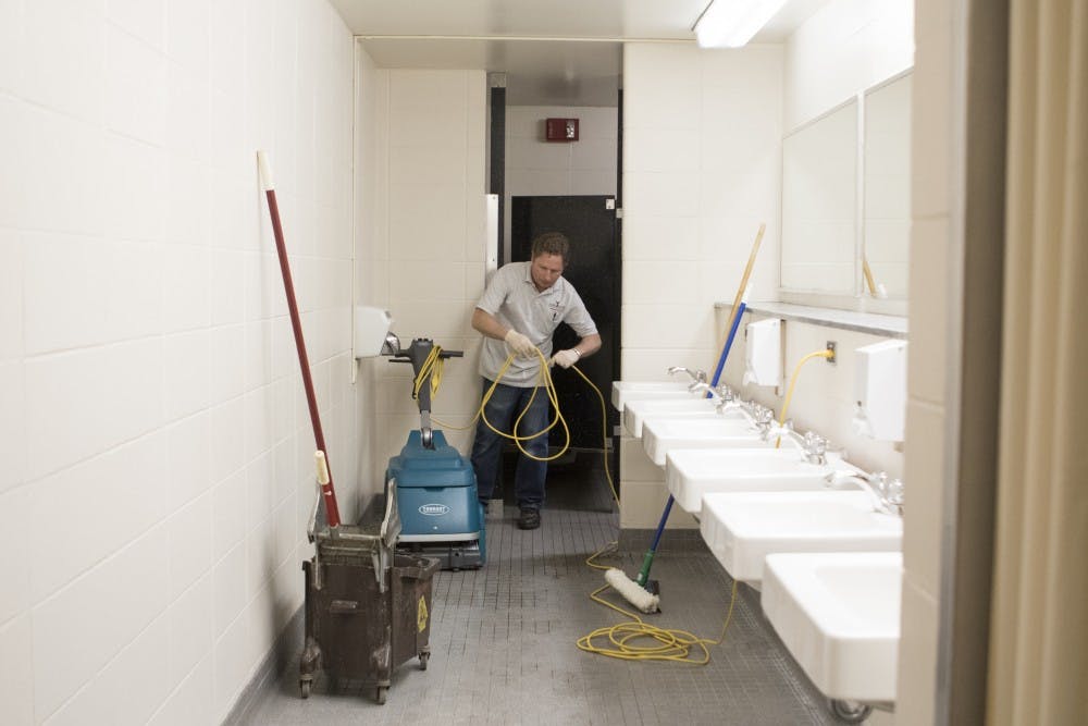 Custodian Greg Hobson mops and cleans one of the men's bathrooms on the LaFollette Complex's first floor. With the students gone, Hobson has the chance to scrub and wax the stairwells and landings.DN PHOTO JORDAN HUFFER