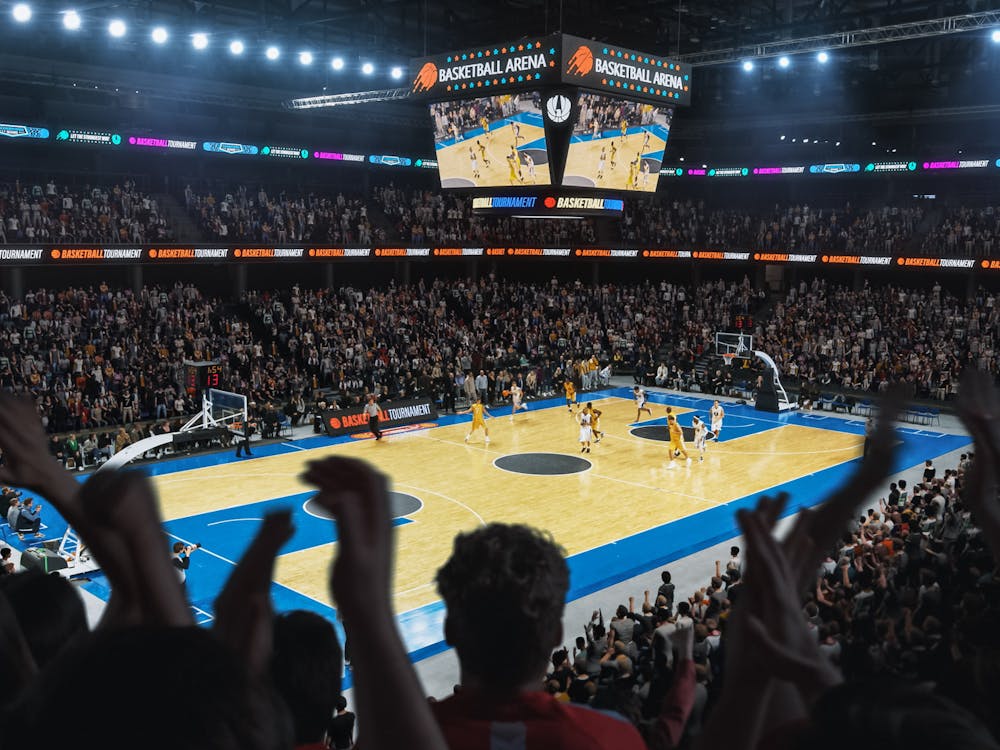 High Angle Establishing Wide Shot of a Whole Arena of Spectators Watching a Basketball Championship Game. Teams Play, Crowds of Fans Raise Hands and Cheer. Sports Channel Live Television Broadcast