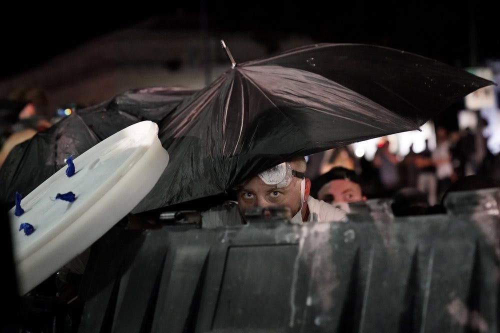A protester takes cover during clashes outside the Kenosha County Courthouse late Tuesday, Aug. 25, 2020, in Kenosha, Wis., during a third night of unrest following the shooting of a Black man whose attorney said he was paralyzed after being shot multiple times by police. (AP Photo/David Goldman)
