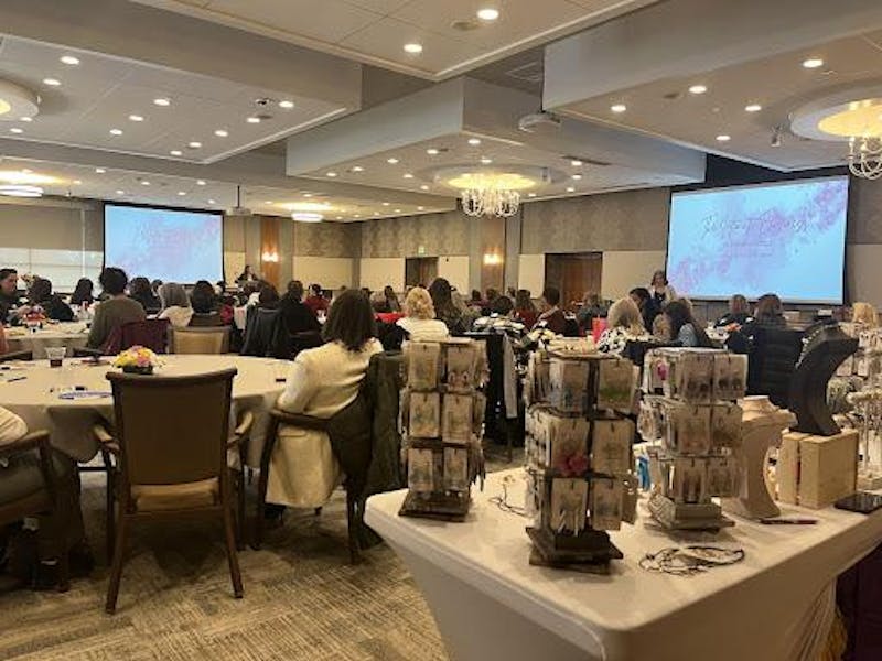 A spacious room with attendees seated at tables, focused on presentations displayed on large screens at the front.