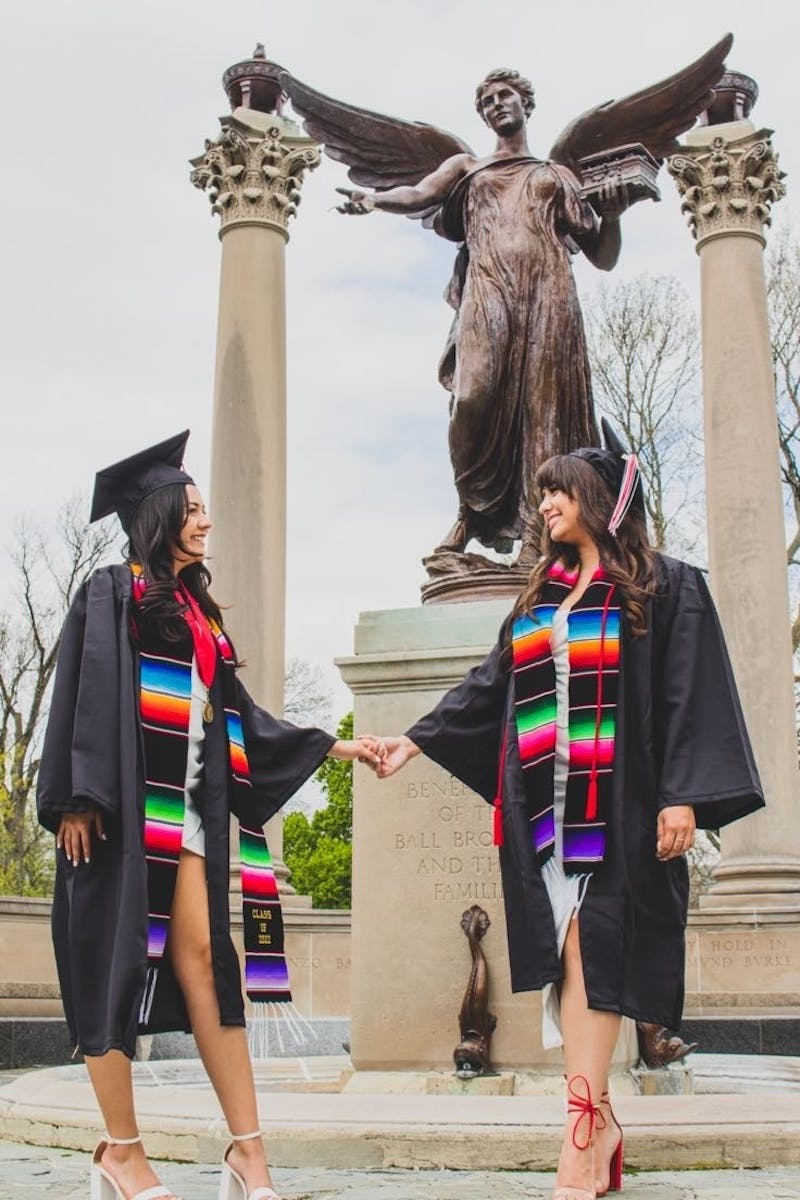 Spring 2022 Ball State University graduate Abril Castaneda and her friend pose with Beneficence on Ball State's campus in Muncie, Indiana. The women are dressed in their cap and gowns they will wear during the commencement ceremony May 7. 