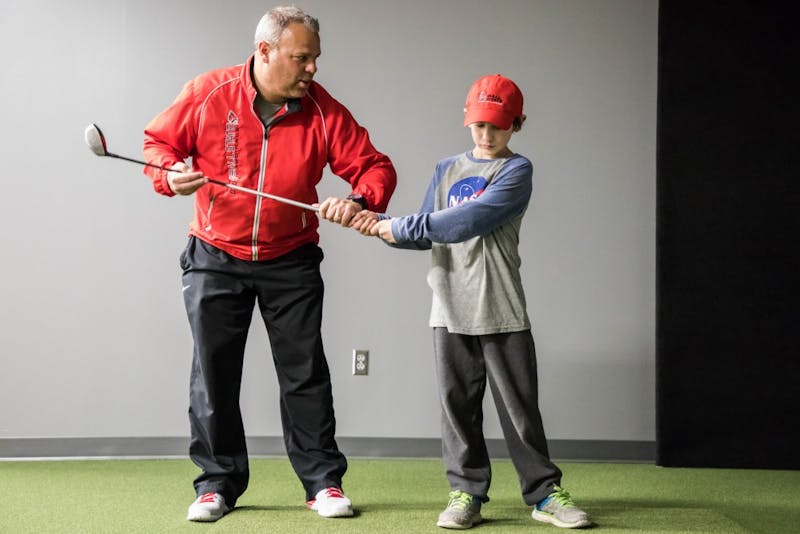 Ball State men's golf head coach Mike Fleck works with Manasseh Crum on his swing Jan. 23 at the Travis Smith Short Game Center. Crum has Polyarticular Juvenile Idiopathic Arthritis. He is part of Team IMPACT, a national non-profit organization that connects children facing serious or chronic illnesses with college athletic teams. Rachel Ellis, DN