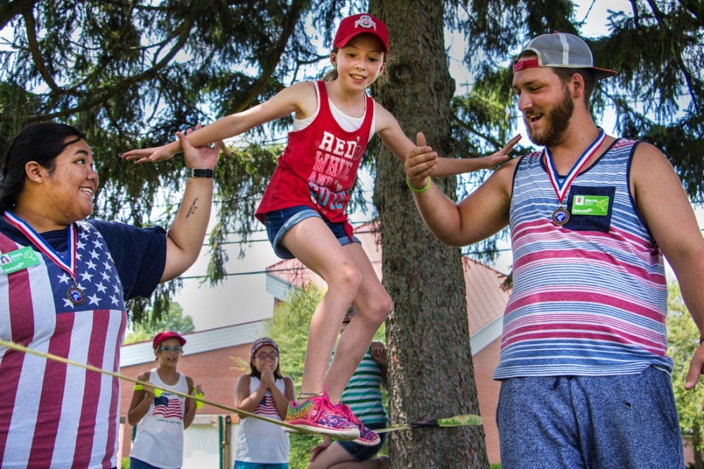 Counselors Jenny Pacurib and Derric Gowan guide Sarah, a SpringHill camper, across a slack line on July 27 at Reynoldsburg United Methodist Church in Ohio. Grace Ramey // SpringHill Camps