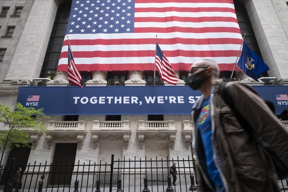 A man wearing a protective face mask passes the New York Stock Exchange, May 26, 2020, as employees arrive for the partial reopening of the trading floor. (AP Photo/Mark Lennihan)