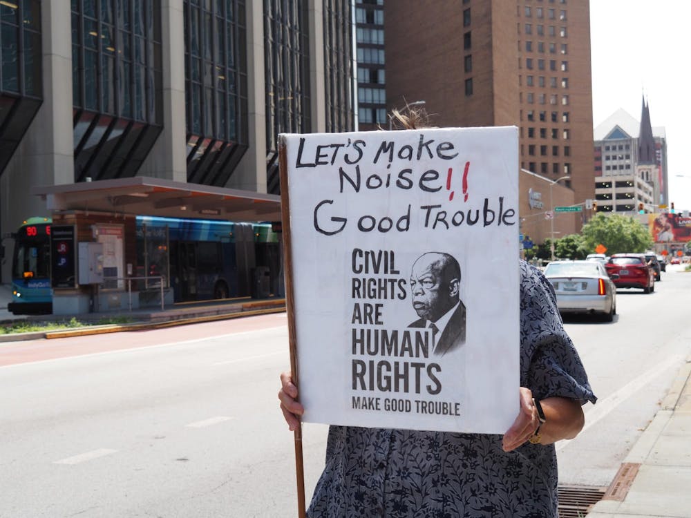������������������������������� A woman holds a “good trouble” sign during a protest of President Donald Trump held outside the Indiana Statehouse on Thursday, July 17, 2025. (Leslie Bonilla Muñiz/Indiana Capital Chronicle)