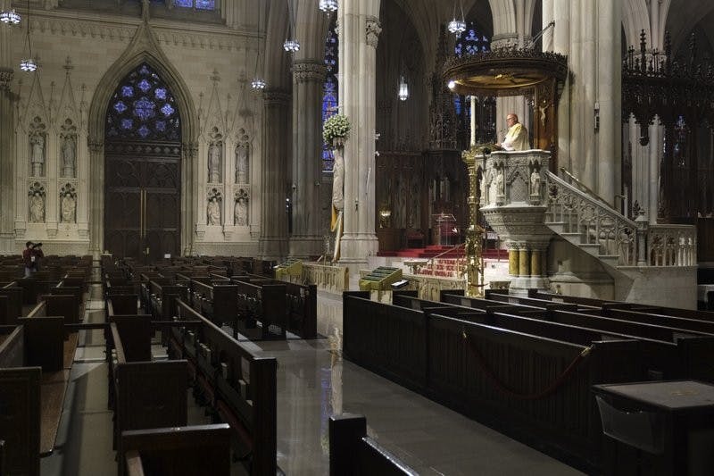 Archbishop Timothy Dolan, right, delivers his homily over empty pews as he leads an Easter Mass at St. Patrick's Cathedral in New York, Sunday, April 12, 2020. Due to coronavirus concerns, no congregants were allowed to attend the Mass but it was broadcast live on a local TV station. AP Photo/Seth Wenig