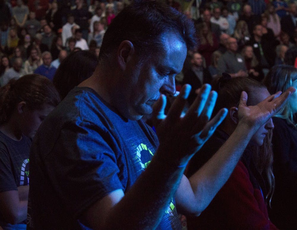 A man bows his head and raises his hands up in the air during a moment of prayer at the Fileds of Faith Nov. 1, 2018, at Worthen Arena. The event began at 6:30 p.m. Patrick Murphy, DN