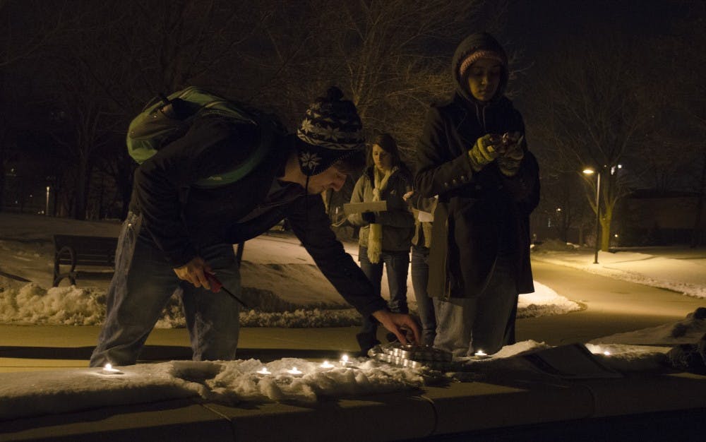 Sophomore environmental science major Derek Tepe reaches for a candle to light during the vigil as a part of a nationwide movement to protest the Keystone XL Pipeline. Senior psychology major Ariana Brown lights a candle next to Tepe during the vigil at Frog Baby on Monday. Around 10 students participated in the vigil and they walked around campus to pass out fliers. DN PHOTO BREANNA DAUGHERTY 