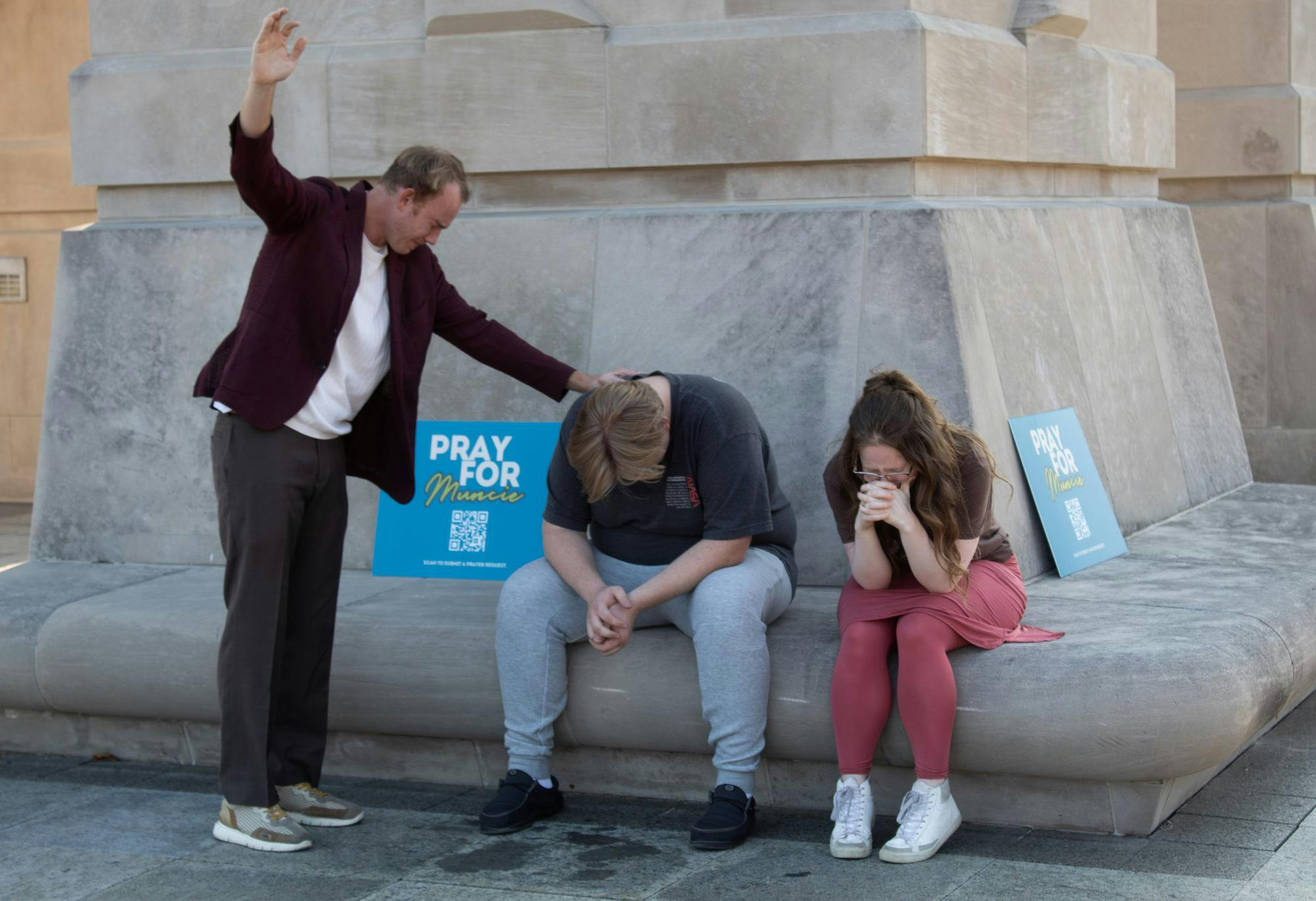 Pastor of River Life Church Riley Martin prays for two Muncie Prayer event attendees, sitting on the base of Schafer Tower at Ball State University Sept. 11th in Muncie, Ind. Titus Hood, DN