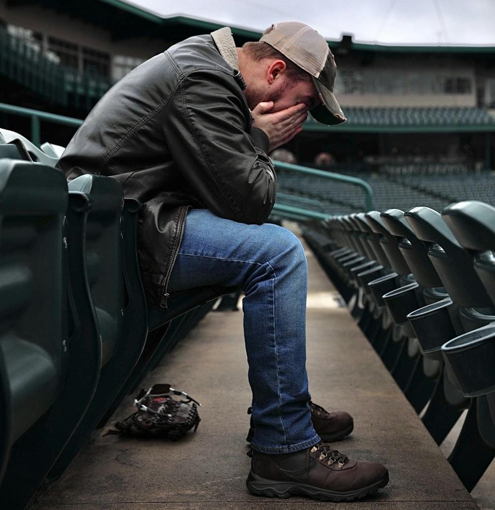 <p>Zach Piatt sits with his head in his hands March 22, 2020, at Parkview Field in Fort Wayne, Indiana. “Anytime I walk into an empty sports venue, something feels off,” Piatt said. “It's not right. It's supposed to be buzzing.” <strong>Jacob Musselman, DN Illustration</strong></p>