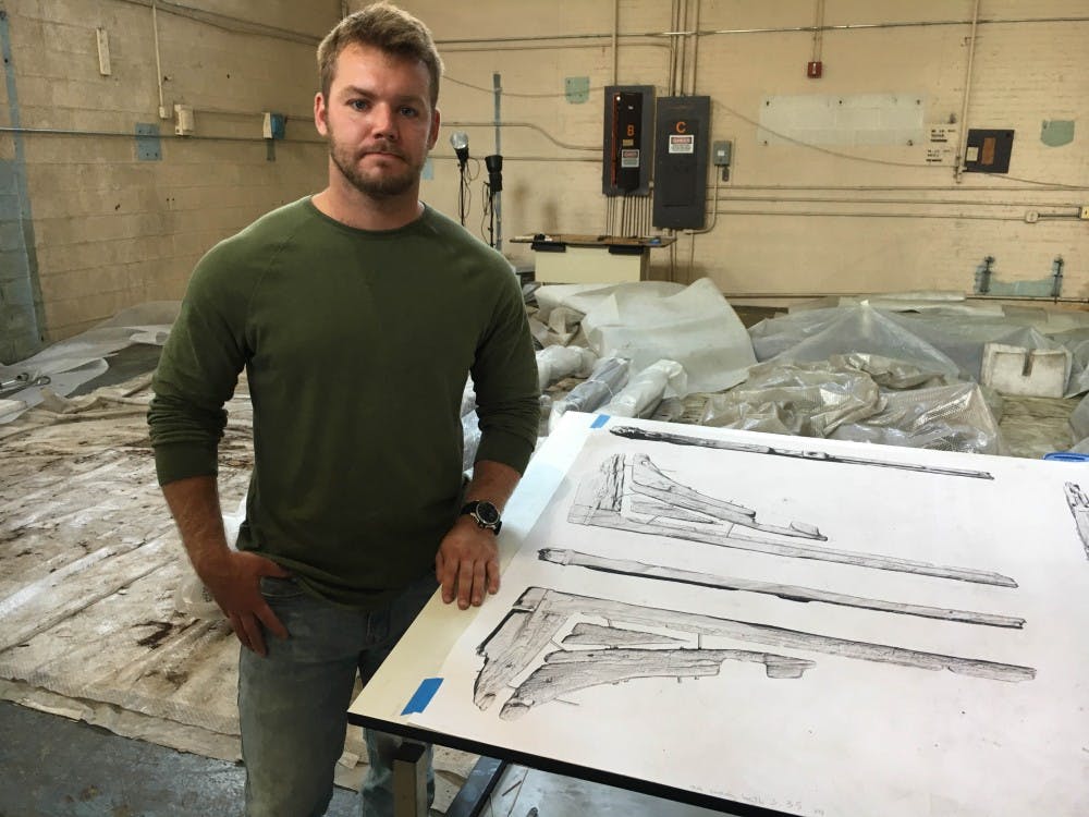 <p>Senior Anthropology and History Major Evan Olinger stands next to a 3D rendering of a colonial-era ship's timbers at the Washington Navy Yard during his internship over the summer. <strong>Photo Provided</strong></p>