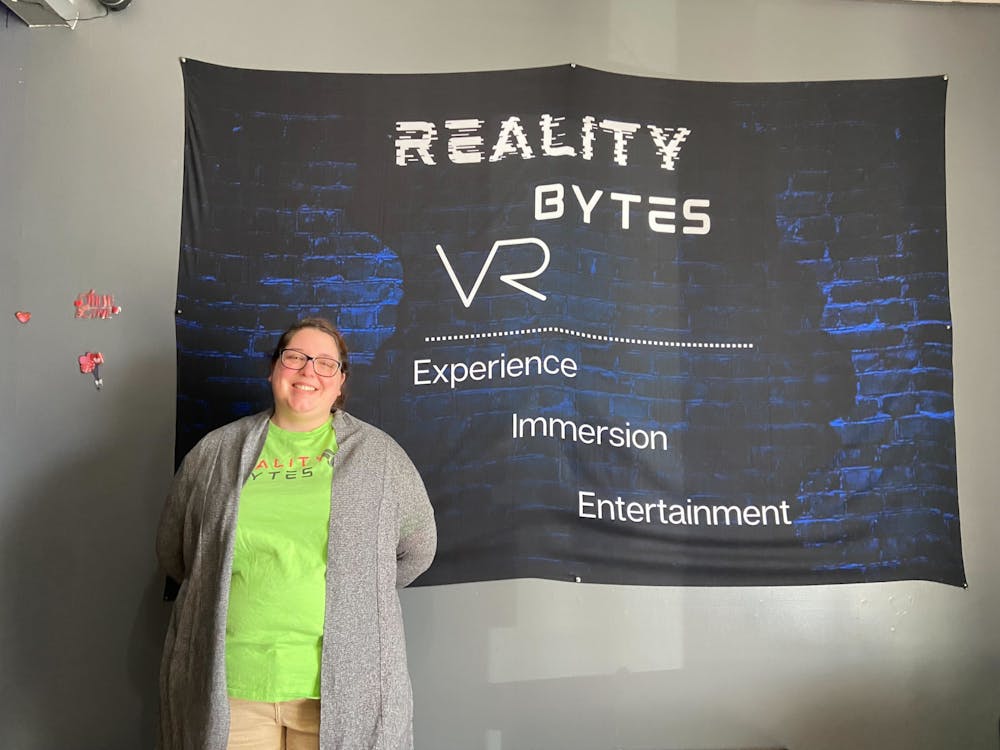 Reality Bytes owner Beth Rizzo poses in front of a poster at the entrance of the shop Saturday, Feb. 4. Reality Bytes has been open since July 2022. Lila Fierek, DN