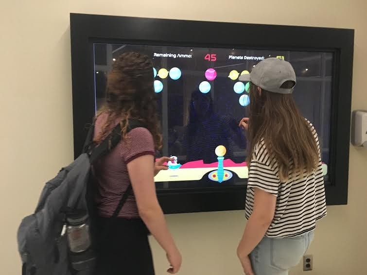 Freshman telecommunications major Sam Essex and sophomore telecommunications and design technology major Selena Webb play "Charlie Destroys Worlds" outside of the Digital Corps office. The game was developed this semester by senior animation major Marisa Lozano. Michelle Kaufman // DN