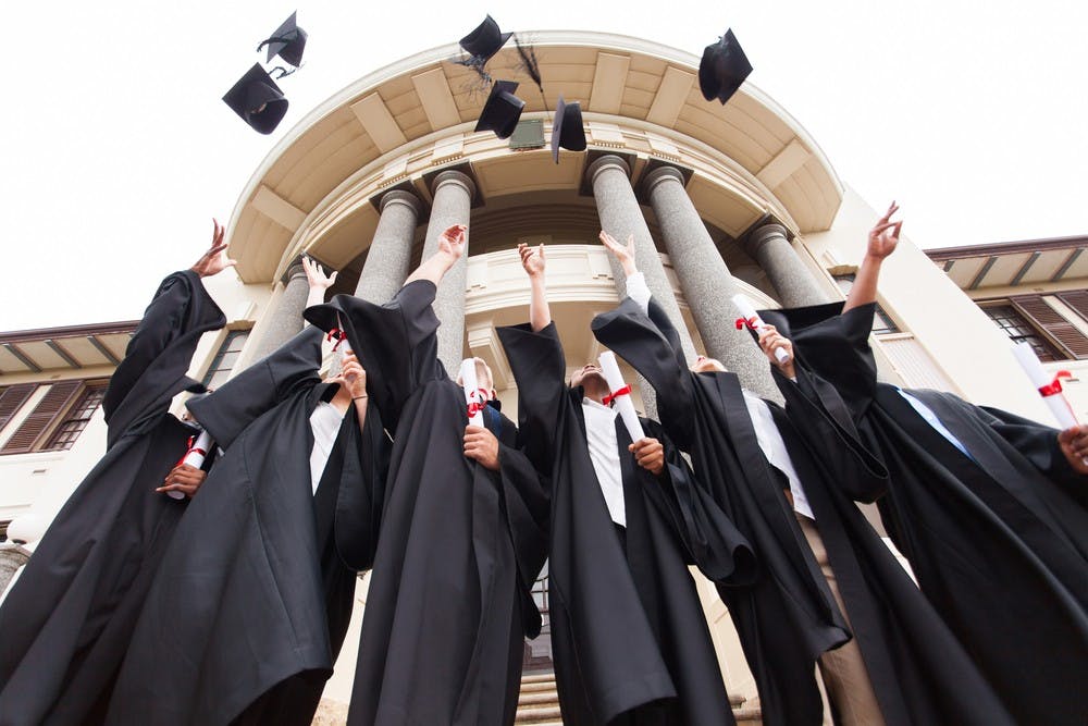 group of happy graduates throwing graduation hats in the air celebrating