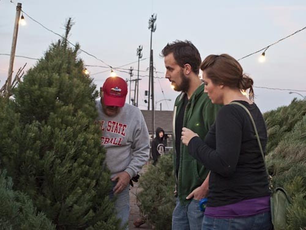 Lot manager and professor emeritus Dave Dixon shows Kyle Beaty and Connie Hoon one of the trees from the lot Monday evening at the Kiwanis tree lot. Kiwanis has been selling the trees since after Thanksgiving and have sold off over half of their lot. DN PHOTO JONATHAN MIKSANEK