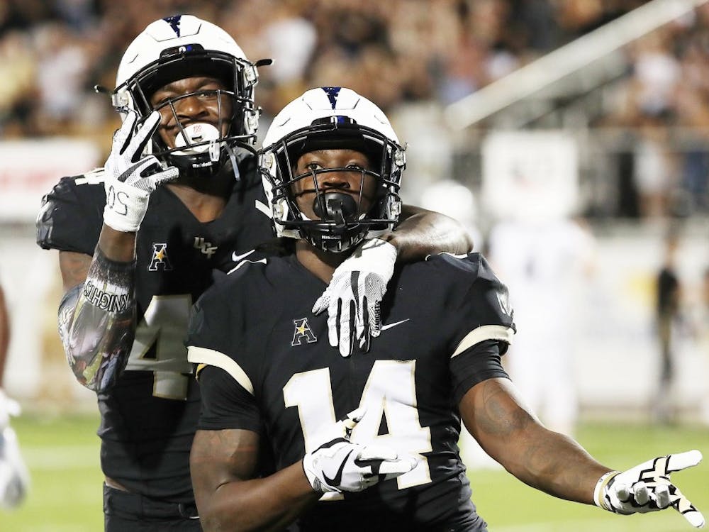 UCF defensive back Nevelle Clarke (14) and linebacker Nate Evans (left) celebrate after Clarke returned an interception for a touchdown during the UConn at UCF football game at Spectrum Stadium in Orlando on Saturday, September 2, 2019. (Stephen M. Dowell/Orlando Sentinel/TNS)