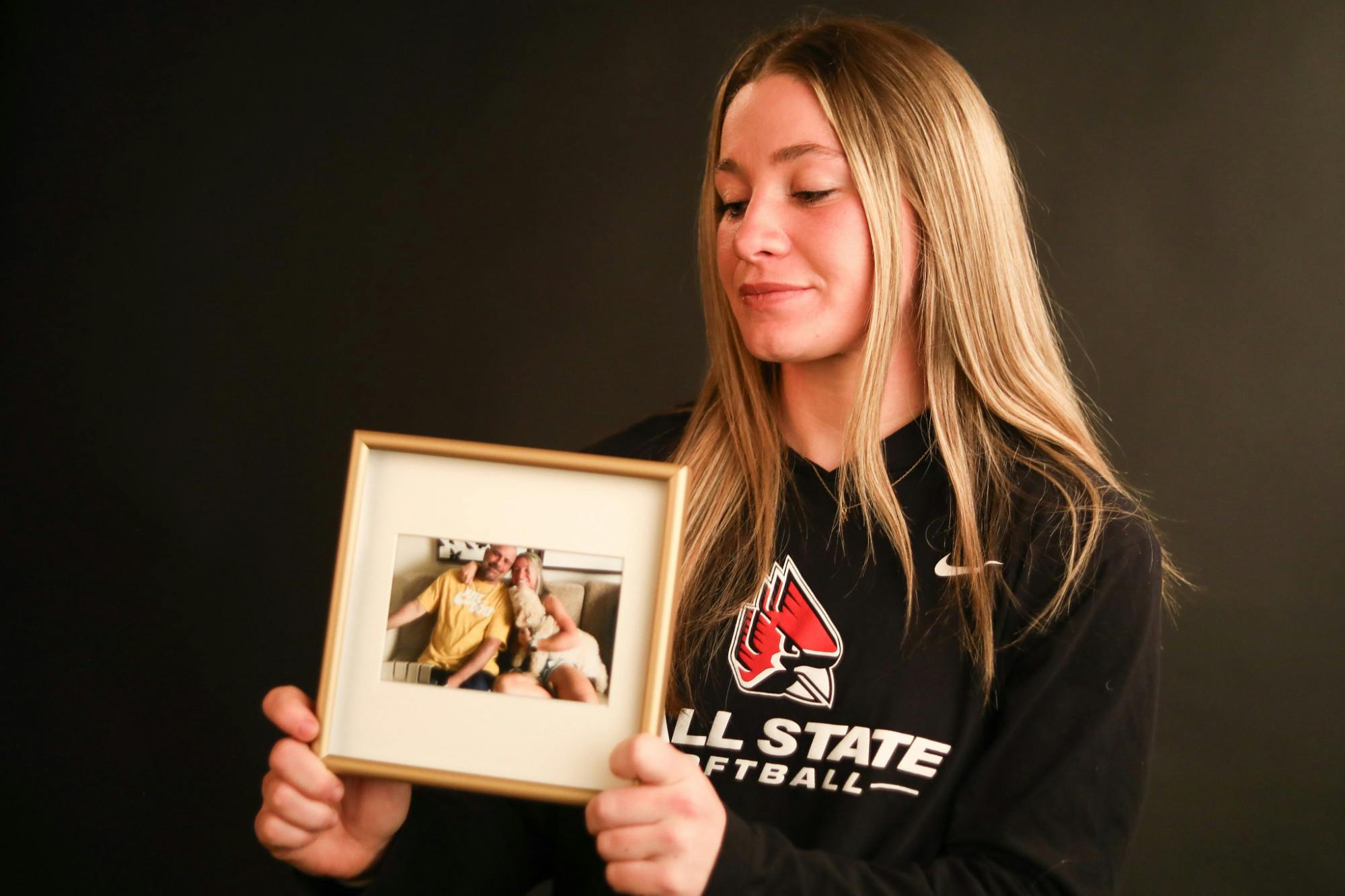 Ball State junior softball player McKenna Mulholland holds an old photo of her and her stepfather on March 31 at the Arts and Journalism Building. Mulholland lost her stepfather in December 2023, closely followed by the beginning of her next softball season. Andrew Berger, DN