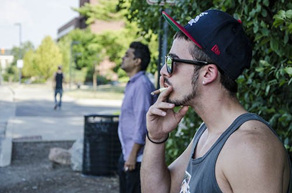 Nathan DeLong, a freshman architecture student, stands smoking a cigarillo on West Petty Road which is right off campus limits. Students and faculty have formed new smoking areas alongside roads flanking the campus to adhere to the new tobacco regulations. DN PHOTO COREY OHLENKAMP