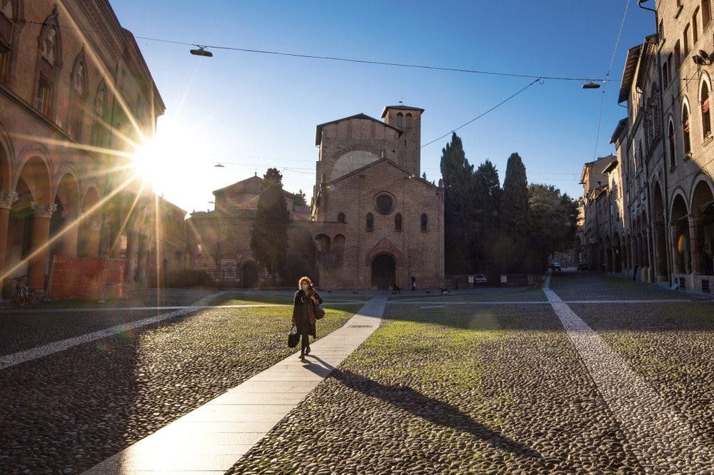 A woman walks past the Basilica of Santo Stefano, March 11, 2020, in Bologna, Italy. In Italy the government extended a coronavirus containment order previously limited to the country’s north to the rest of the country beginning Tuesday, with soldiers and police enforcing bans. For most people, the new coronavirus causes only mild or moderate symptoms, such as fever and cough. For some, especially older adults and people with existing health problems, it can cause more severe illness, including pneumonia. (Massimo Paolone/LaPresse via AP)
