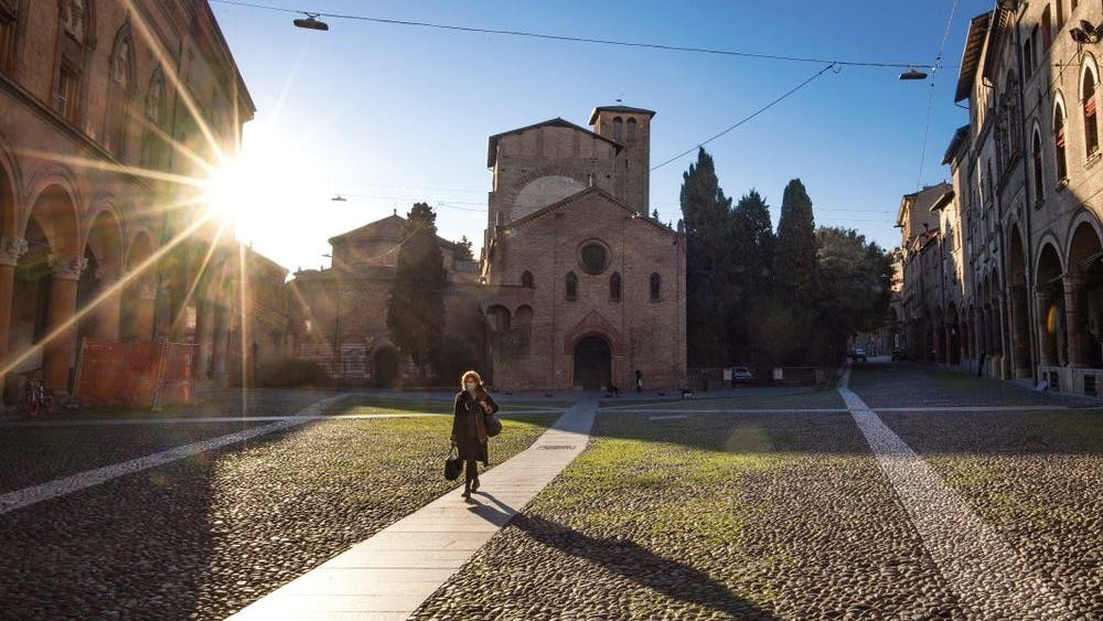 A woman walks past the Basilica of Santo Stefano, March 11, 2020, in Bologna, Italy. In Italy the government extended a coronavirus containment order previously limited to the country’s north to the rest of the country beginning Tuesday, with soldiers and police enforcing bans. For most people, the new coronavirus causes only mild or moderate symptoms, such as fever and cough. For some, especially older adults and people with existing health problems, it can cause more severe illness, including pneumonia. (Massimo Paolone/LaPresse via AP)