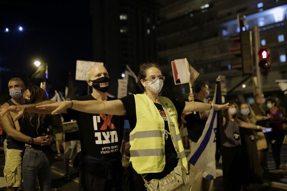 Protesters spread their arms to socially distance in the square outside of Prime Minister Benjamin Netanyahu's residence in Jerusalem, Saturday, Sept. 26, 2020, during a three-week nationwide lockdown in Israel to curb the spread of the coronavirus. (AP Photo/Maya Alleruzzo)