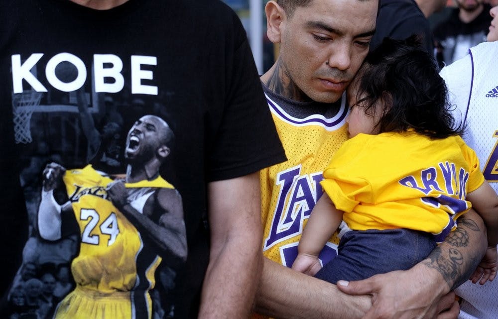 Erik Dominguez holds his 11-month-old daughter Isabella while watching the live stream of a public memorial for Kobe Bryant and his daughter, Gianna, Feb. 24, 2020, outside the Staples Center in Los Angeles. (AP Photo/Ringo H.W. Chiu)