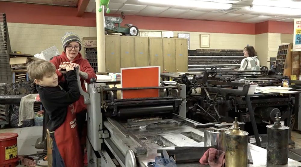 A worker helps a participant roll the poster on a letterpress printer.