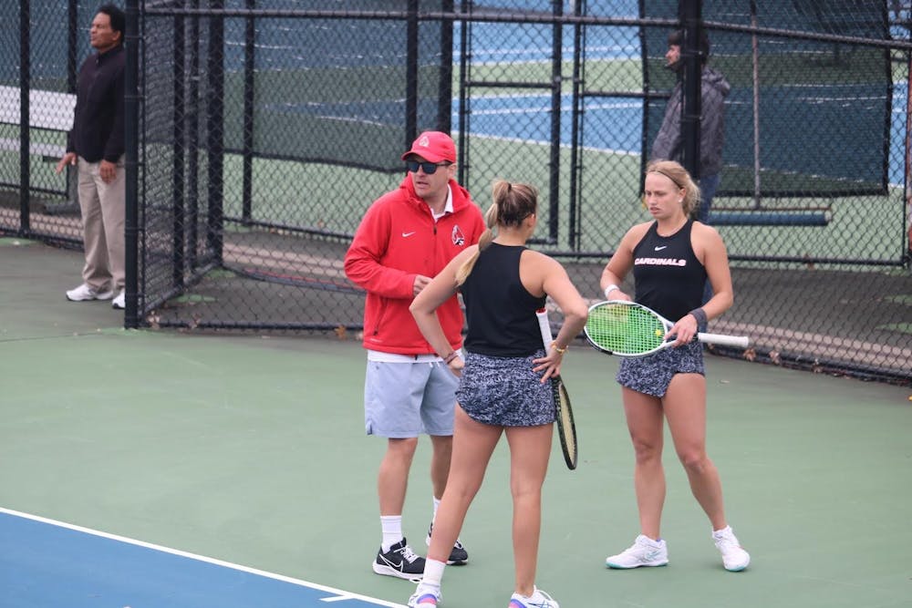 <p>Head coach Max Norris meets with junior Amy Kaplan (left) and senior Hannah Davies (right) in the middle of their doubles match against Buffalo at Cardinal Creek Tennis Courts on April 30, 2022. Their match went unfinished as the Cardinals had already won 2/3 doubles matches en route to a berth in the MAC Championship. Corbin Hubert, DN</p>